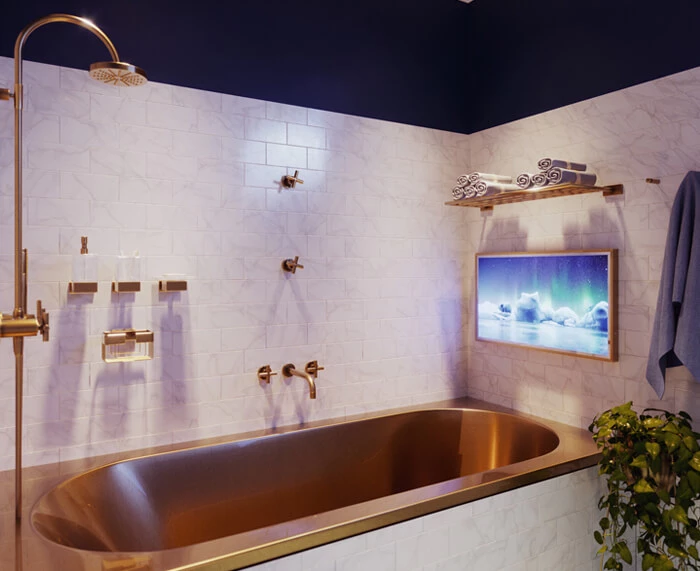 Gold-framed bathtub beneath a framed Ocea Style TV on a white tiled wall in a shower room.